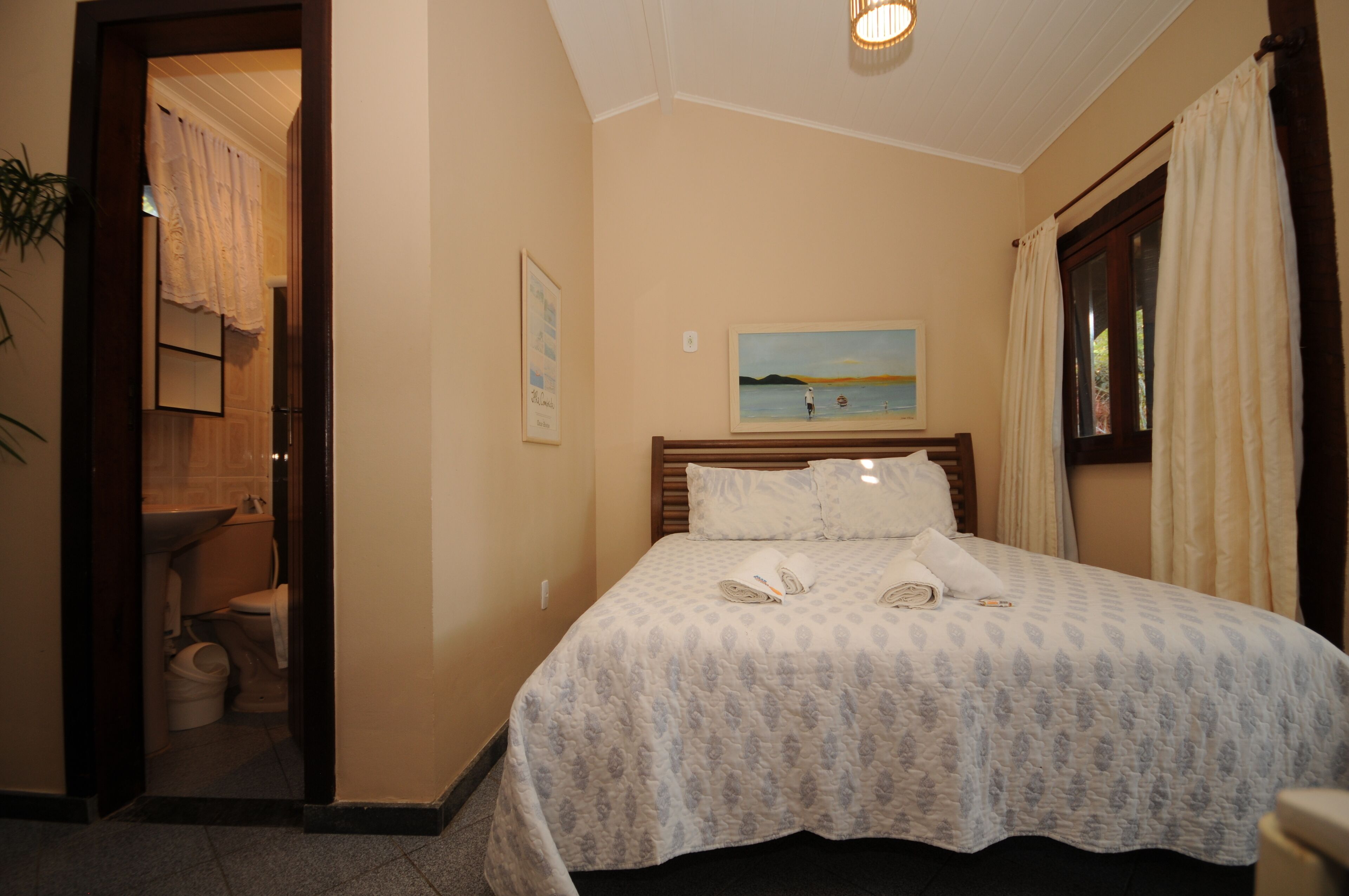 A bedroom with a bed, a painting, and a bathroom visible through an open door.