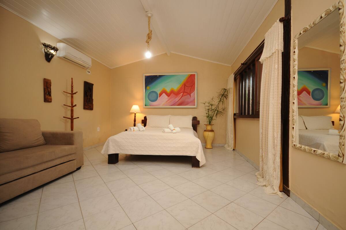 A bedroom with a bed, a sofa, a painting, a lamp, and a mirror.