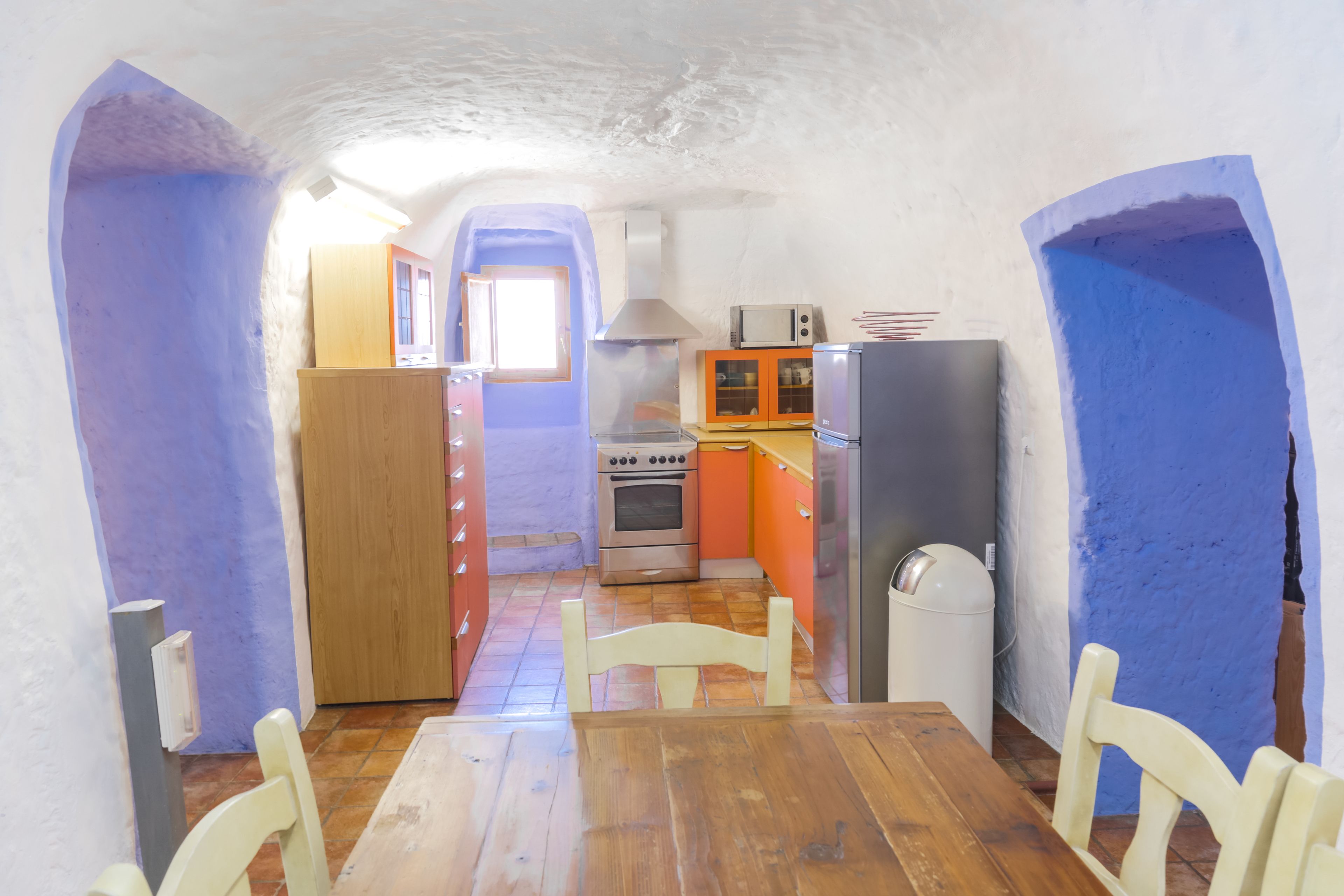 Una cocina compacta con una mesa y sillas de madera, estufa, microondas y refrigerador.