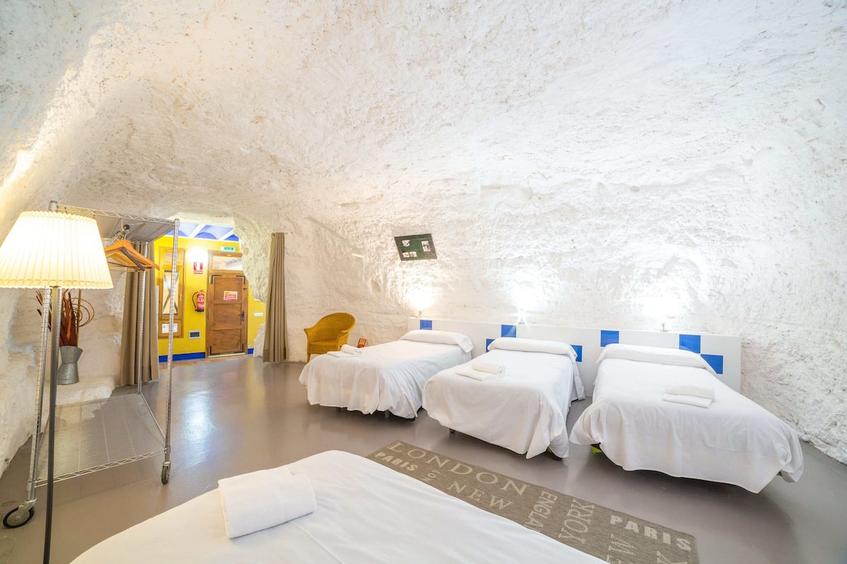 A room with three beds, a lamp, a chair, and a map on the floor.