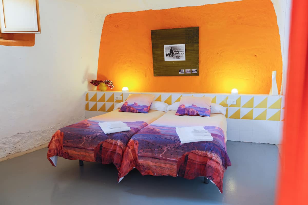 A double bed with patterned bedding, a headboard with a picture, and bedside lamps.