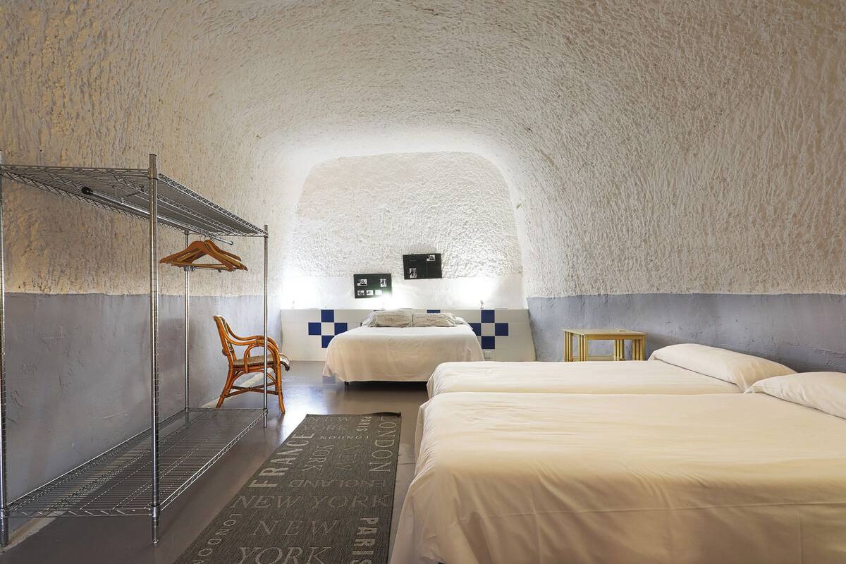 A cozy, arched room with two beds, a hanging clothes rack, a chair, and a small table.