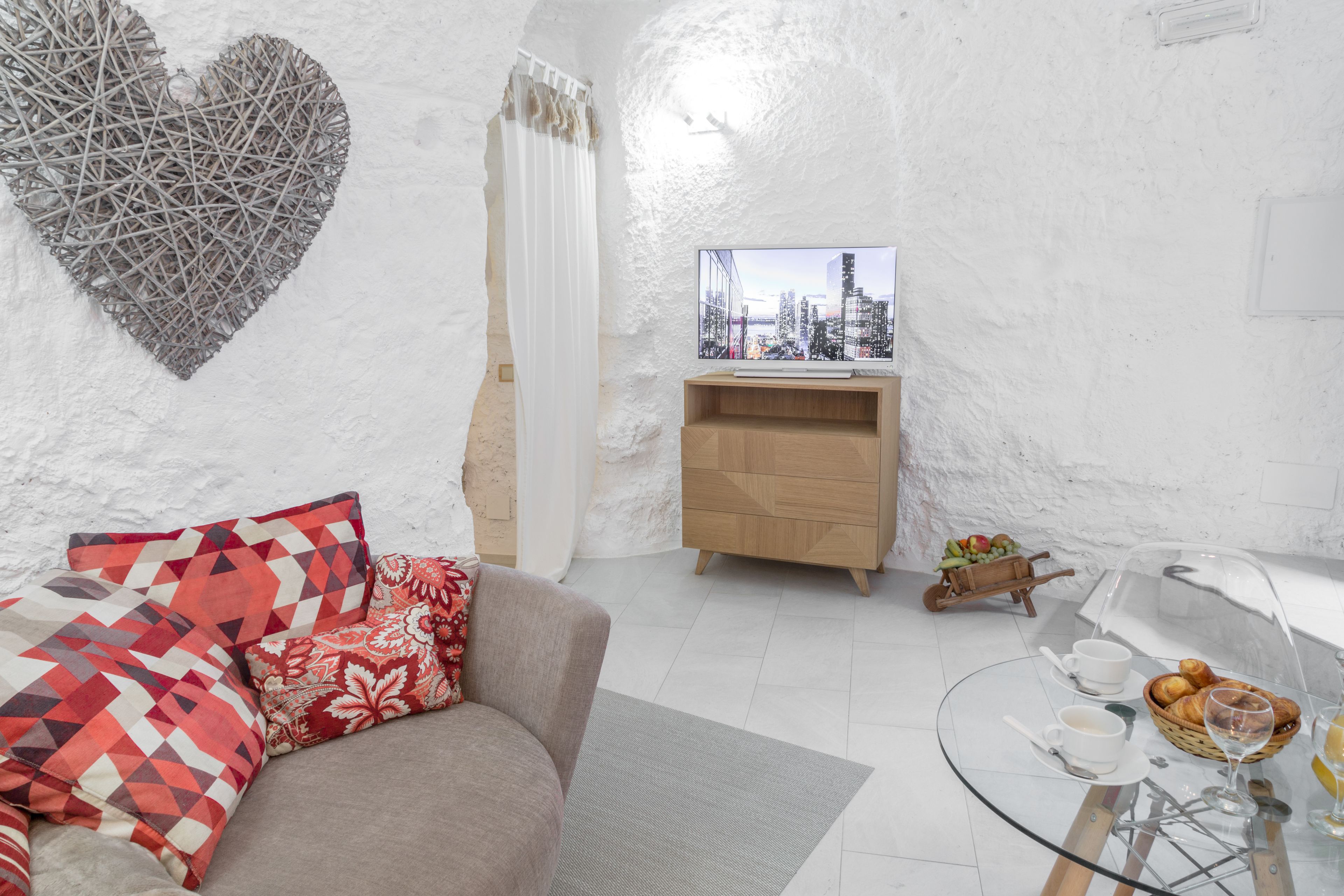 Una sala de estar moderna con un sofá, una mesa de centro de vidrio, un televisor y vistas a un paisaje urbano.