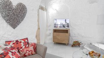 Una sala de estar moderna con un sofá, una mesa de centro de vidrio, un televisor y vistas a un paisaje urbano.