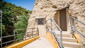 Una escalera lleva a una puerta en un edificio de piedra, con barandilla metálica y ventana.