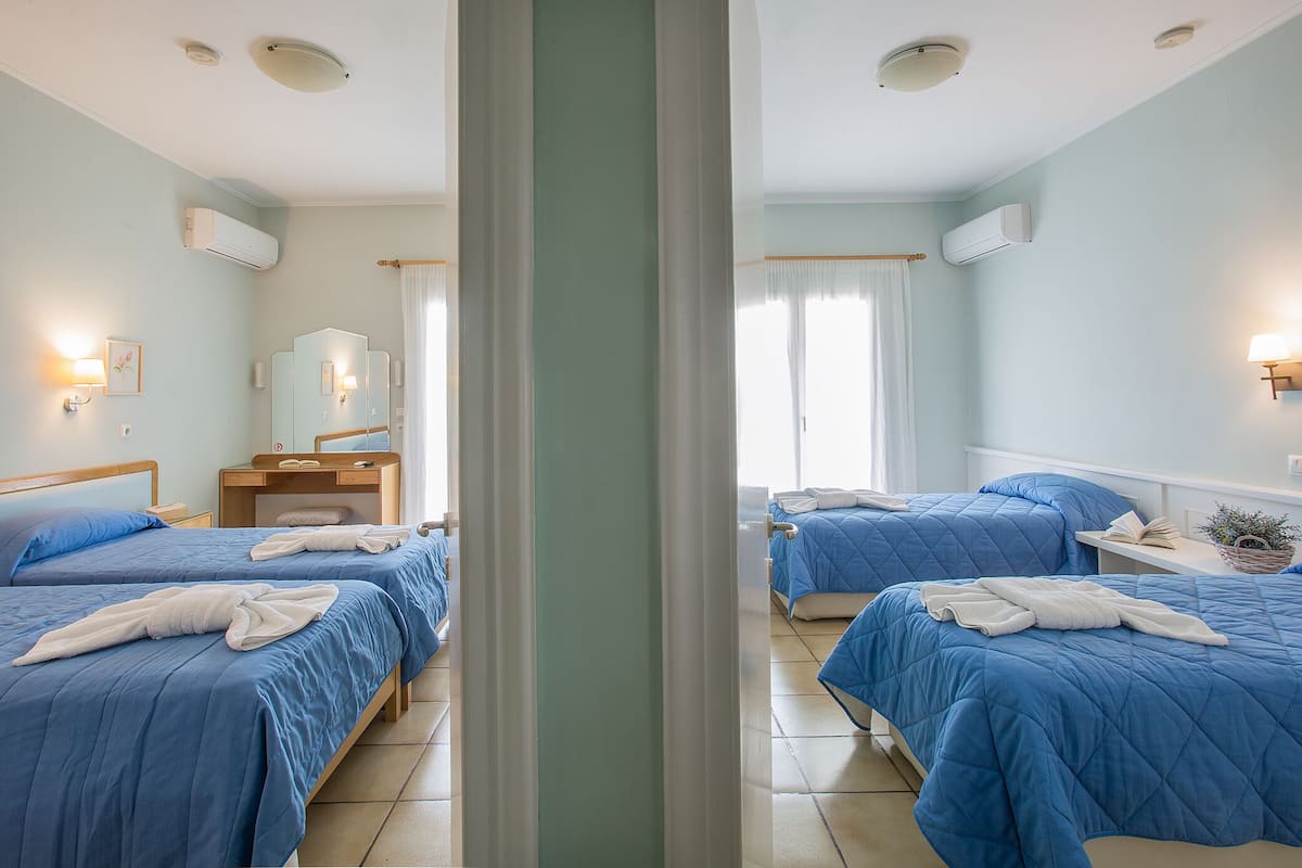 A hotel room with two beds, a wooden nightstand, a mirror, and a window with curtains.
