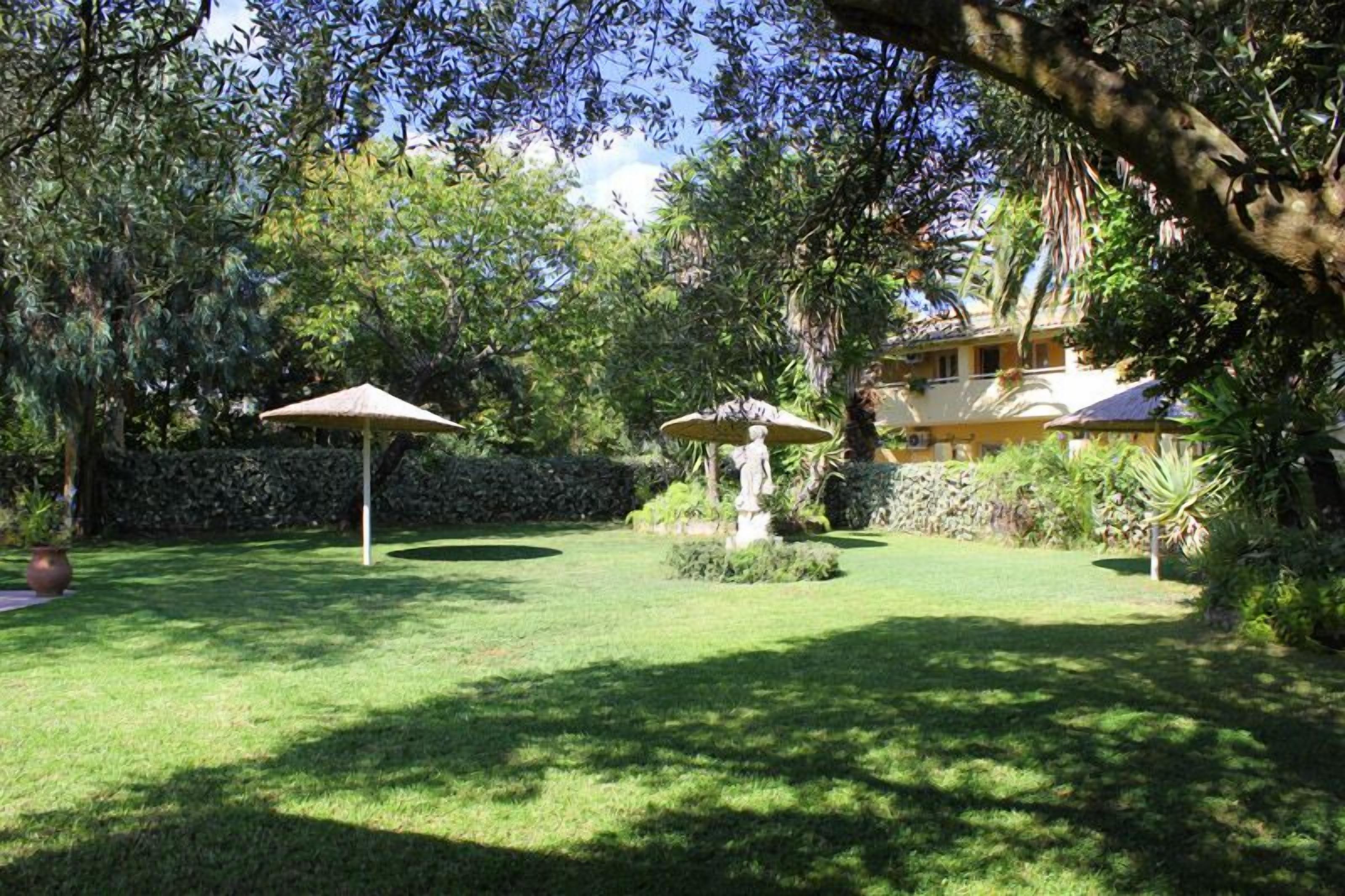 A lush garden with a statue, a gazebo, and a house in the background.
