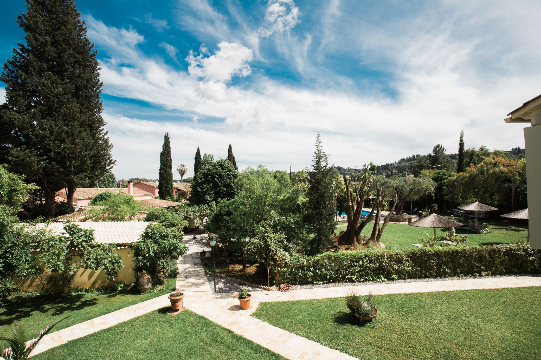 A well-maintained garden with a pathway, potted plants, and a variety of trees.