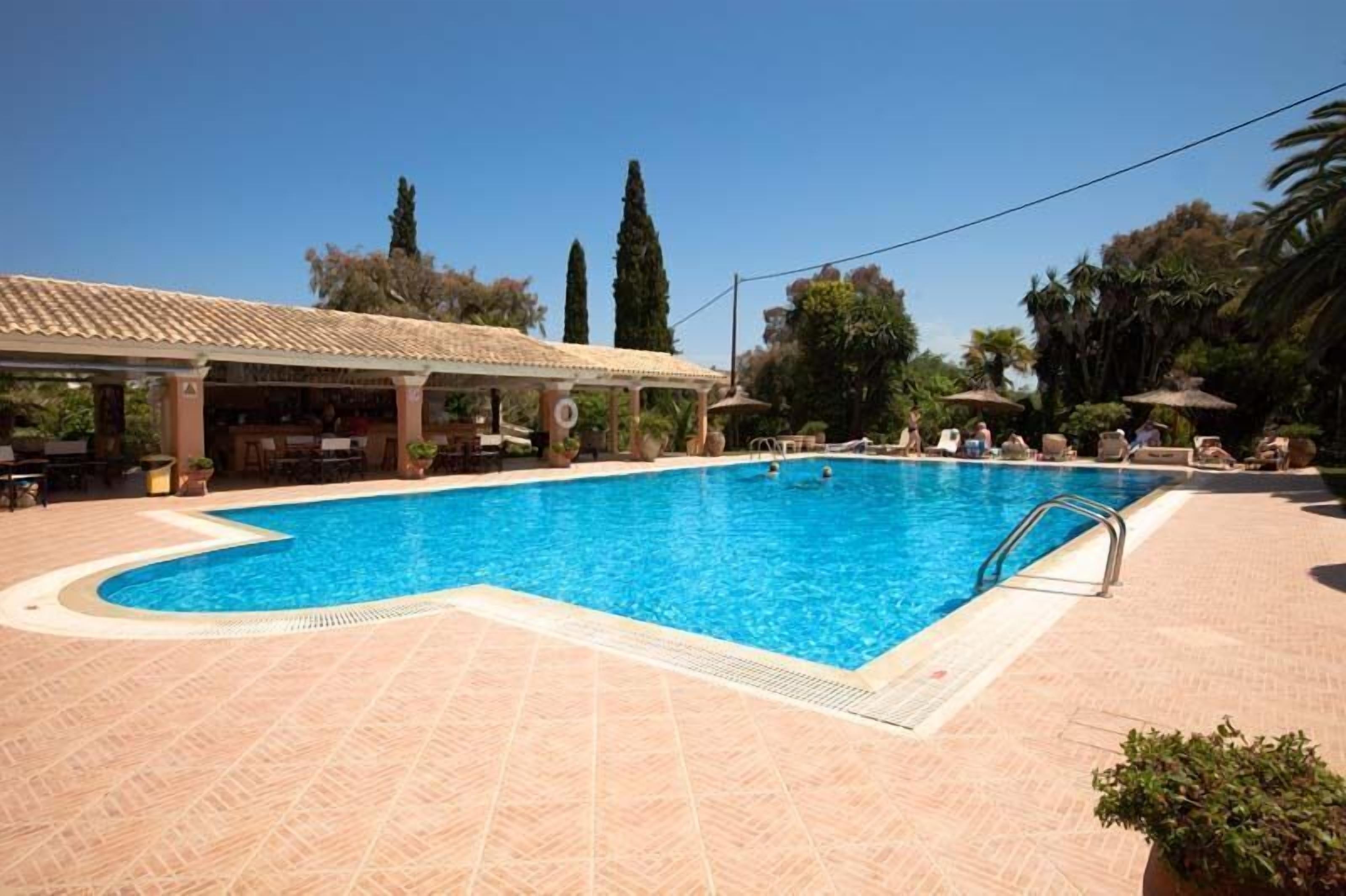 Una piscina con bordo piastrellato, zona relax coperta e vegetazione circostante.