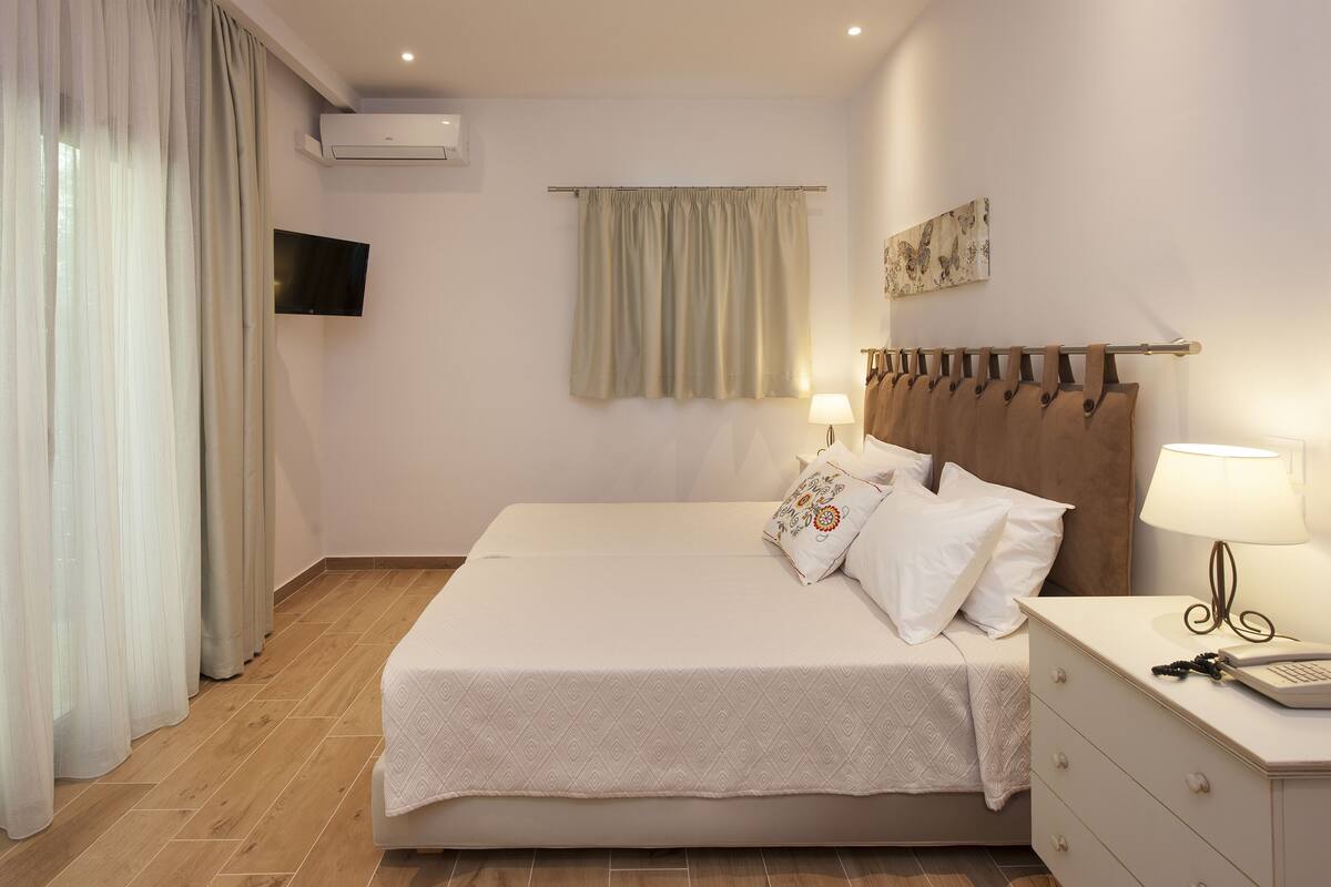 A hotel room with a bed, bedside table, lamp, and a mounted TV.