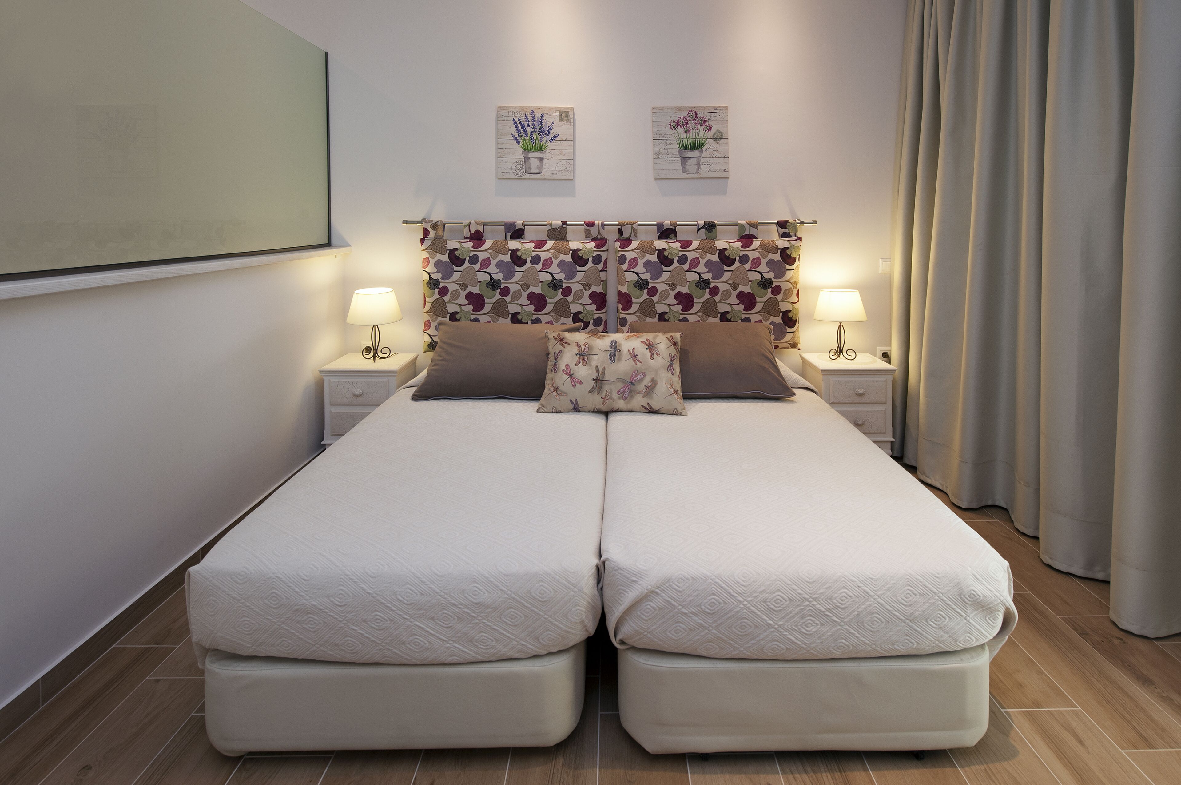 A double bed with a patterned headboard, two bedside tables with lamps, and a large mirror on the wall.