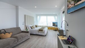 Een moderne hotelkamer met een bed, een bank, een bureau met een laptop en een groot raam.