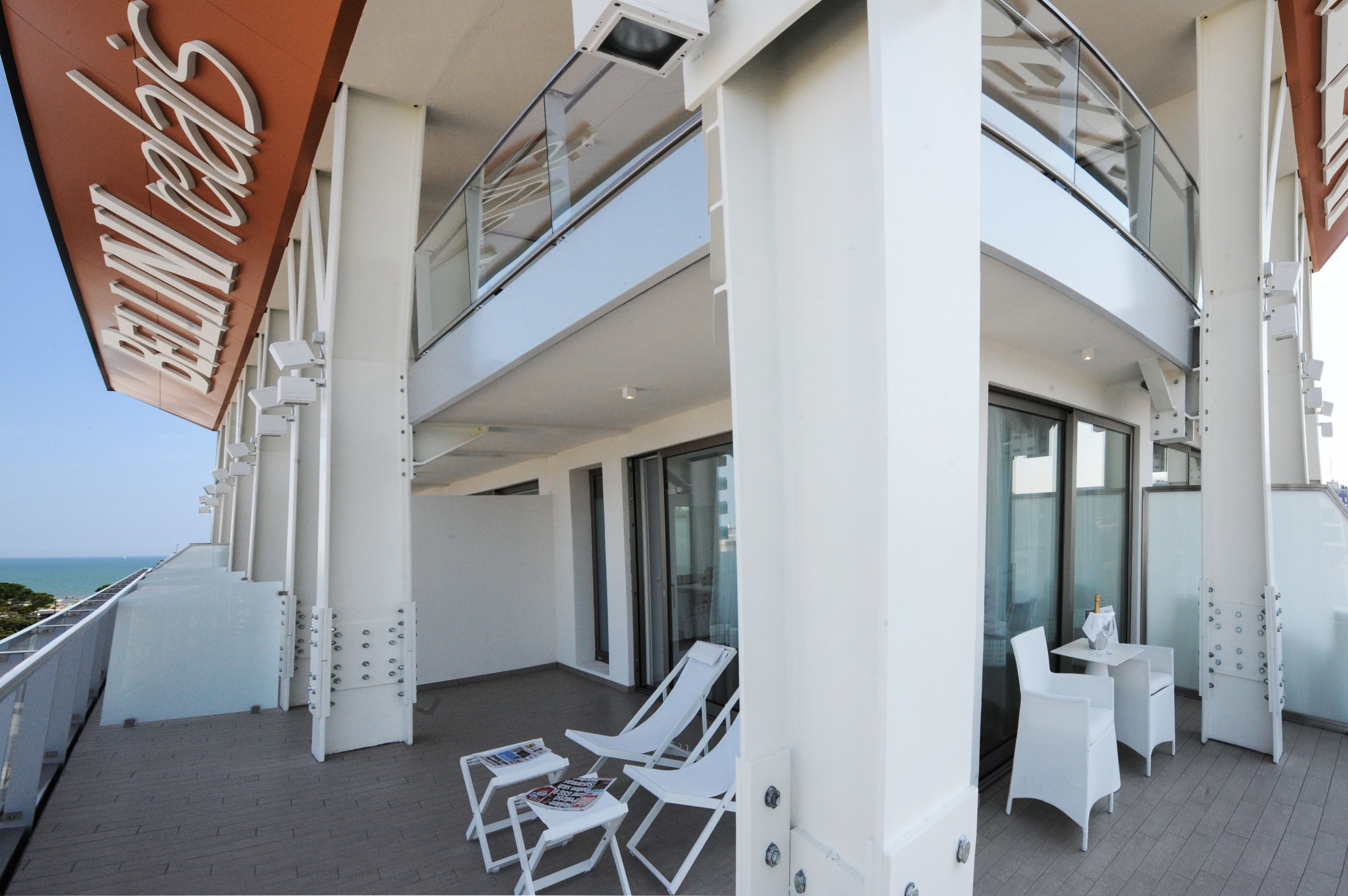 Ein Sonnendeck eines Kreuzfahrtschiffs mit weißen Liegestühlen, einem Glasgeländer und freiem Blick aufs Meer.