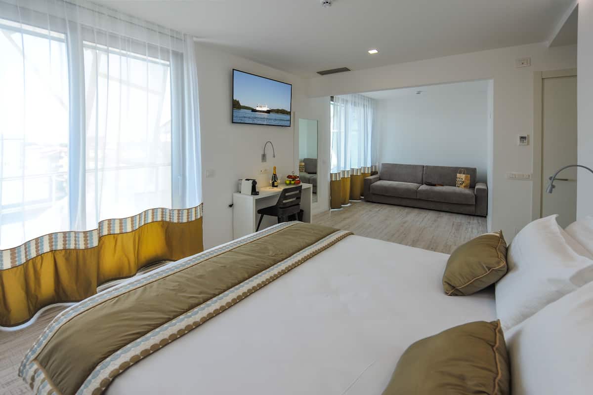 Une chambre d’hôtel avec un grand lit, un bureau avec une chaise, un canapé et une vue sur la mer par la fenêtre.
