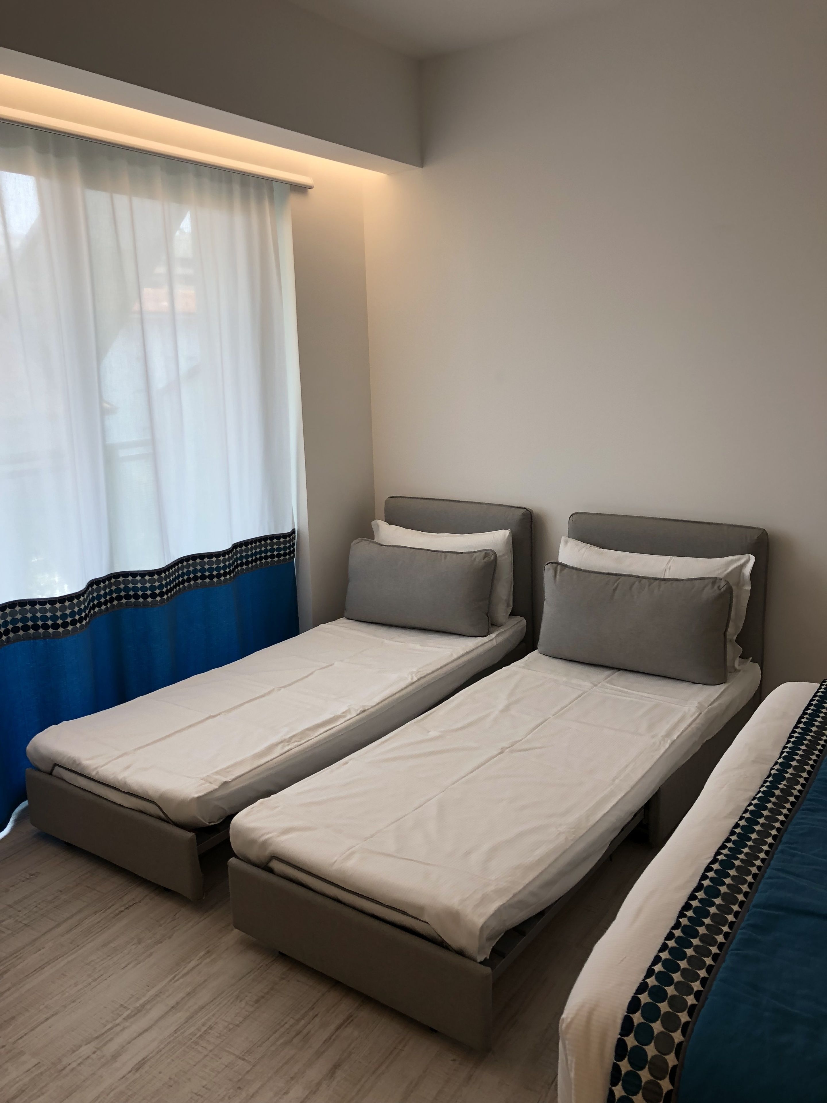 A room with two single beds, a window with sheer curtains, and a patterned bed runner.
