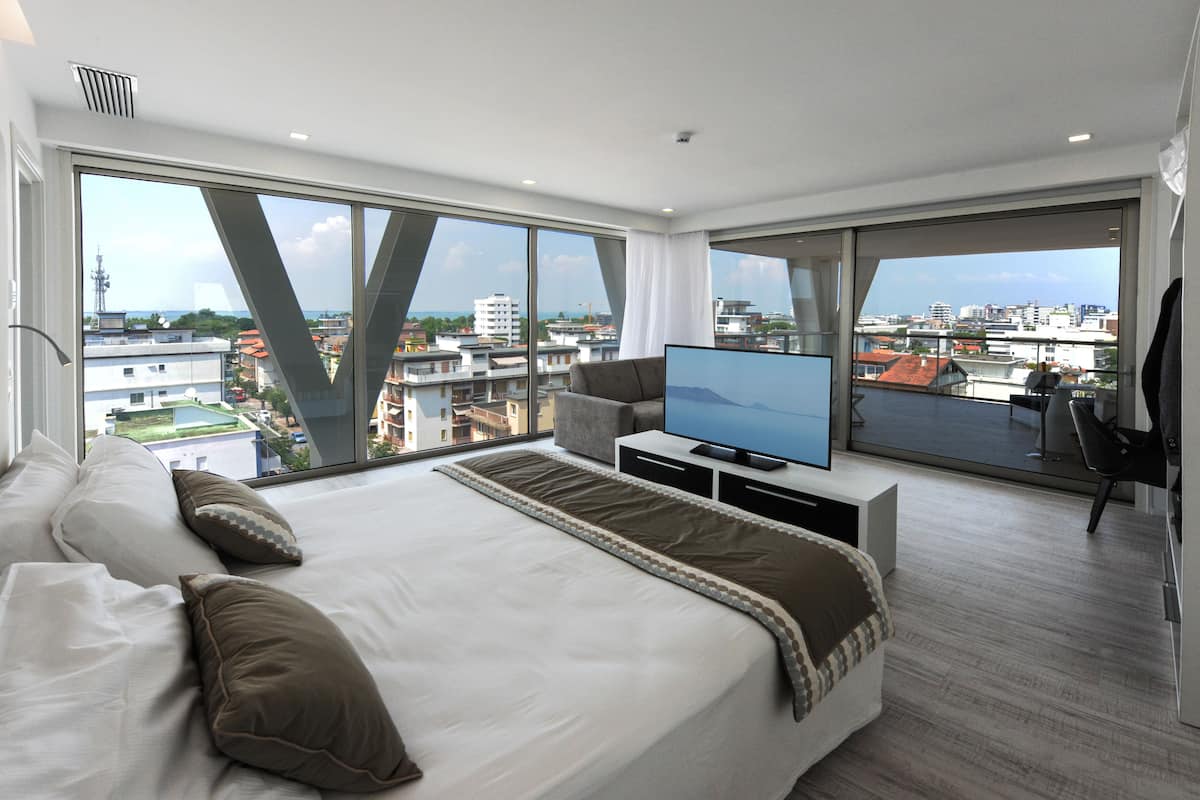 Une chambre d’hôtel moderne dotée d’un grand lit, d’une télévision à écran plat et d’un balcon offrant une vue sur la ville.