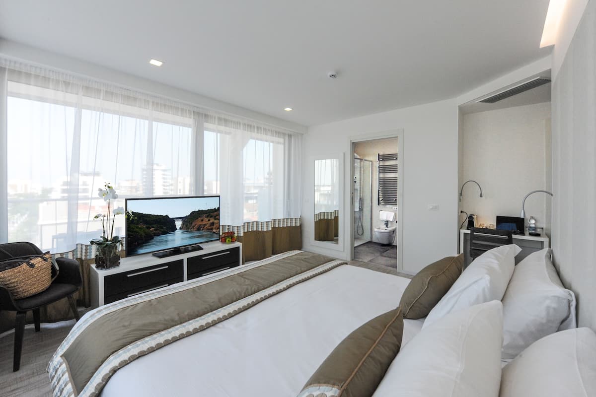 Une chambre d’hôtel moderne, dotée d’un grand lit, d’une télévision, d’un bureau avec un ordinateur et d’une salle de bain visible à travers une porte ouverte.