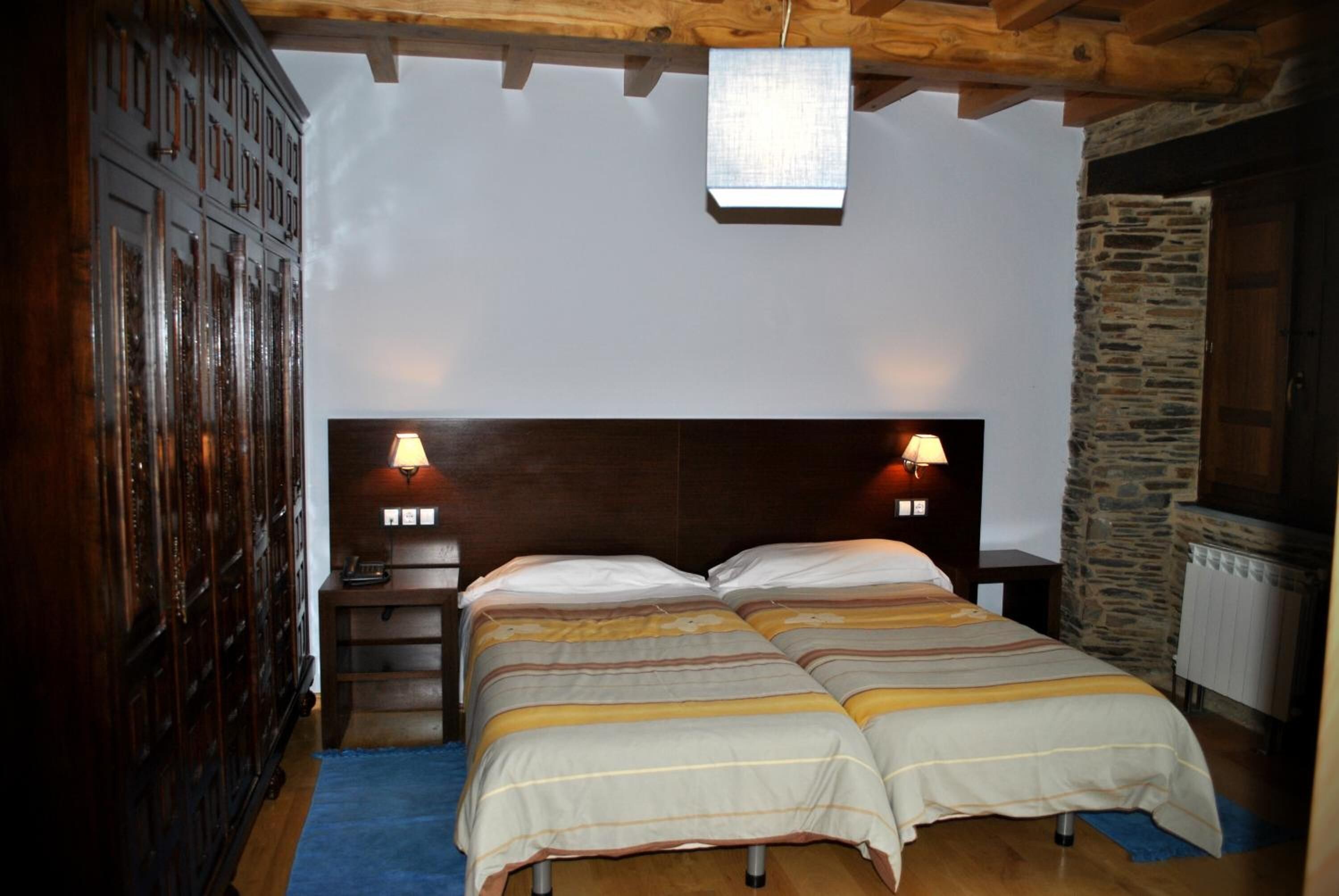 Un lit double avec deux tables de chevet, une armoire en bois et un mur en pierre.
