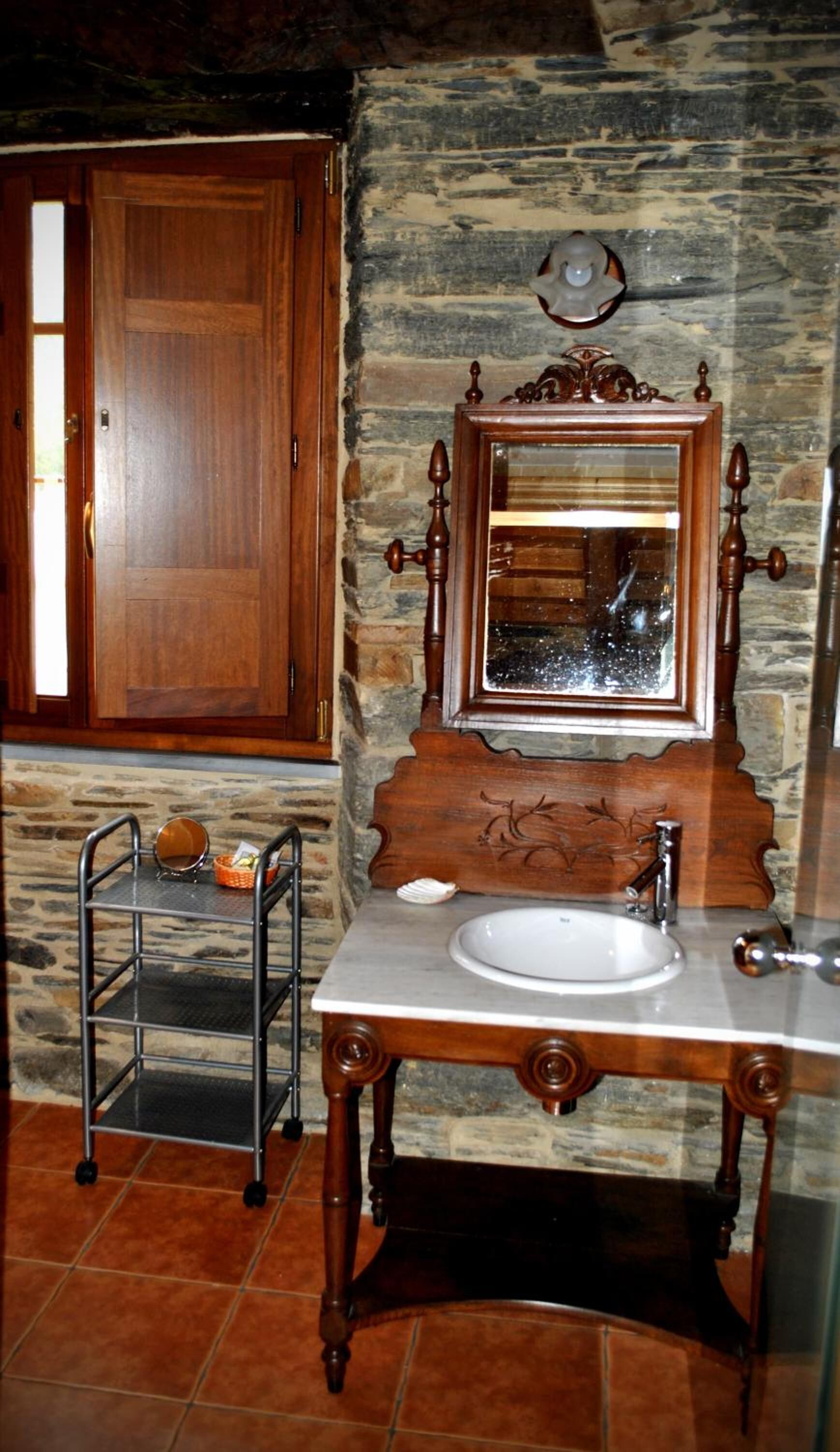 Un baño con tocador de madera, lavamanos, espejo con marco decorativo y estante metálico.
