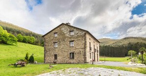 A stone building with a sloped roof, multiple windows, and a paved entrance area. - Finca O Bizarro (Trabada)