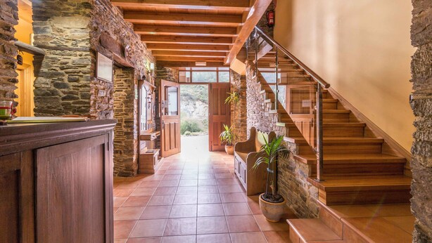 A stone-walled hallway with a wooden staircase leading to a second floor.
