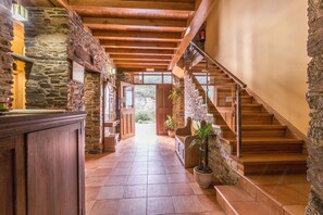 A stone-walled hallway with a wooden staircase leading to a second floor. - Finca O Bizarro (Trabada)