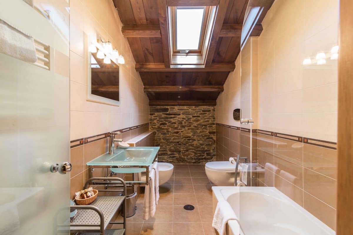 A bathroom with a stone wall, a glass sink, a bathtub, and a skylight.