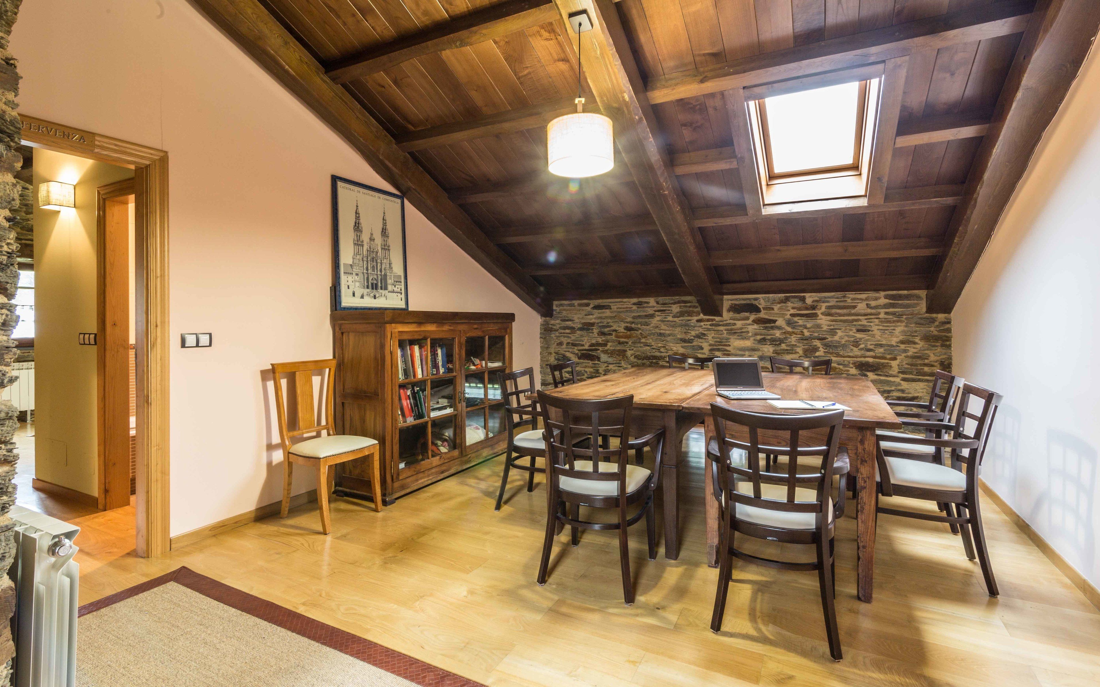 A rustic dining area with a wooden table and chairs, a stone wall, and a skylight.