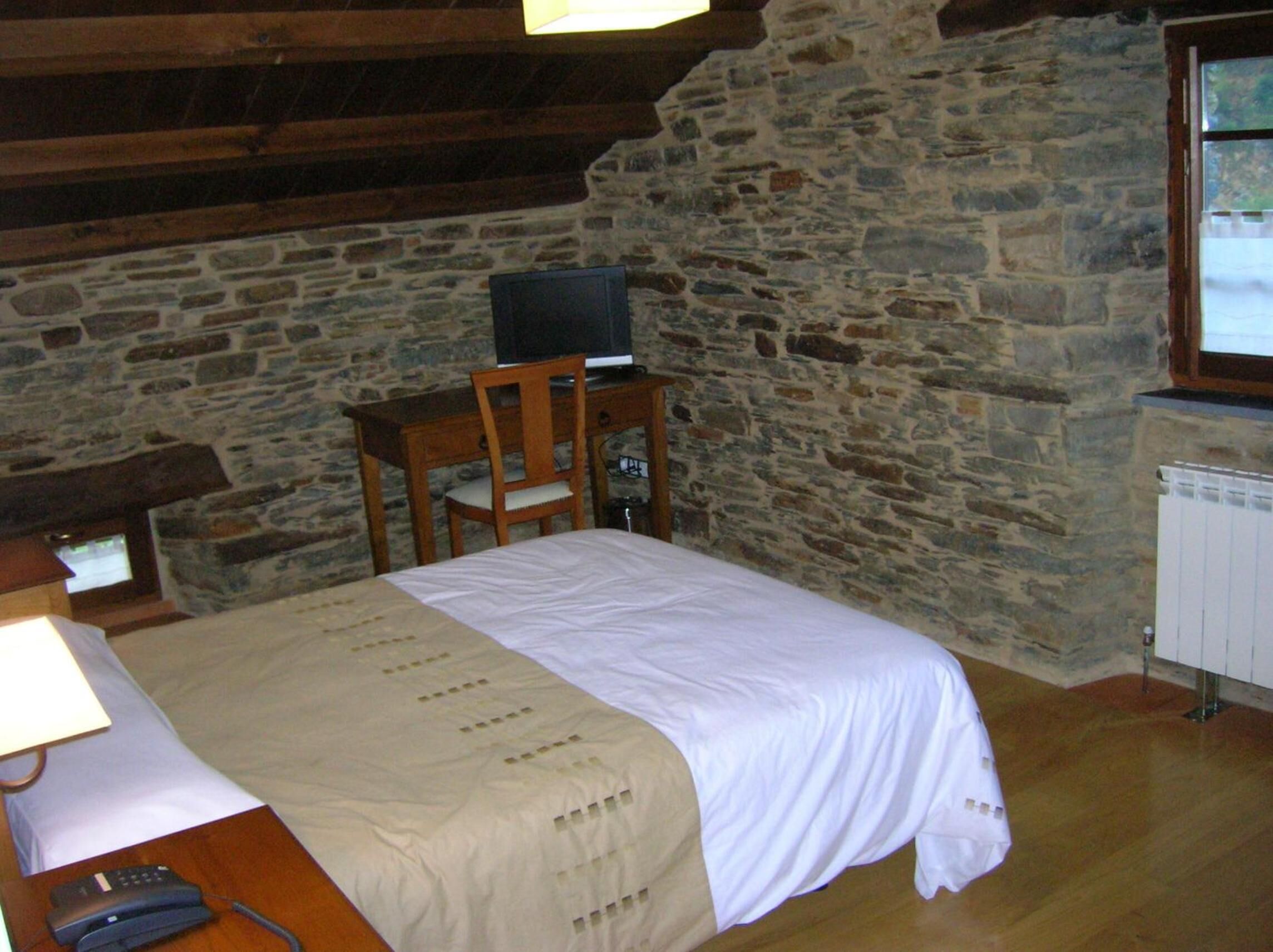 Una habitación con cama, escritorio con computadora, silla y ventana con vista.