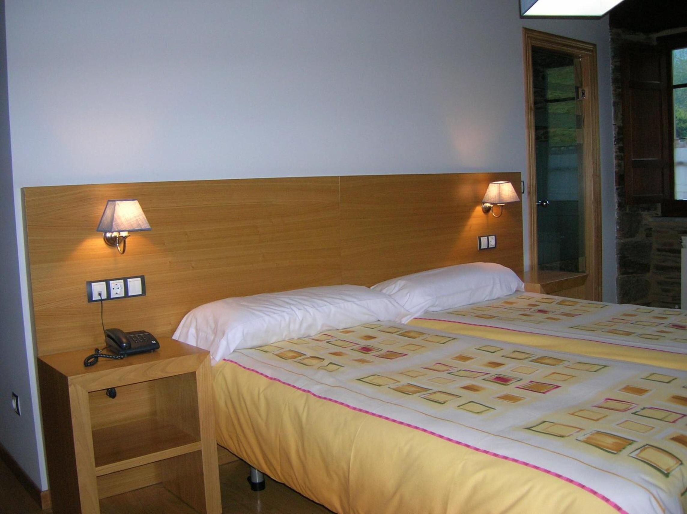 A hotel room with a wooden headboard, two bedside lamps, a telephone, and a bed with a patterned bedspread.