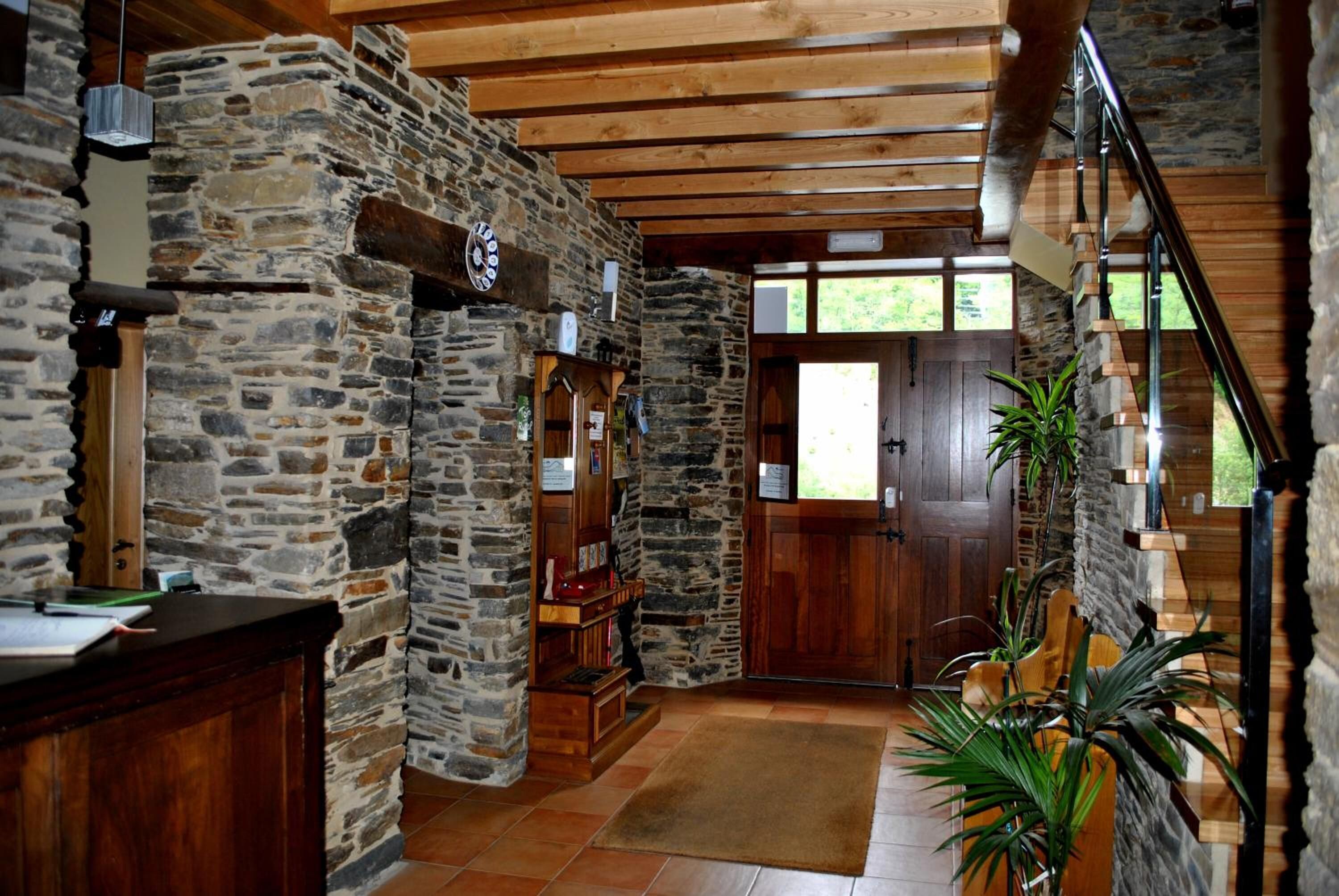 A stone-walled lobby with a wooden reception desk, a wooden staircase, and a door leading outside.