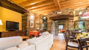 A cozy interior with stone walls, wooden beams, a sofa, dining area, and a TV.