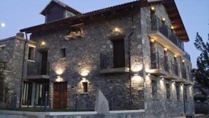 A stone building with multiple windows and a sloped roof, featuring exterior lighting. - Hotel El Churron (Sabinanigo)