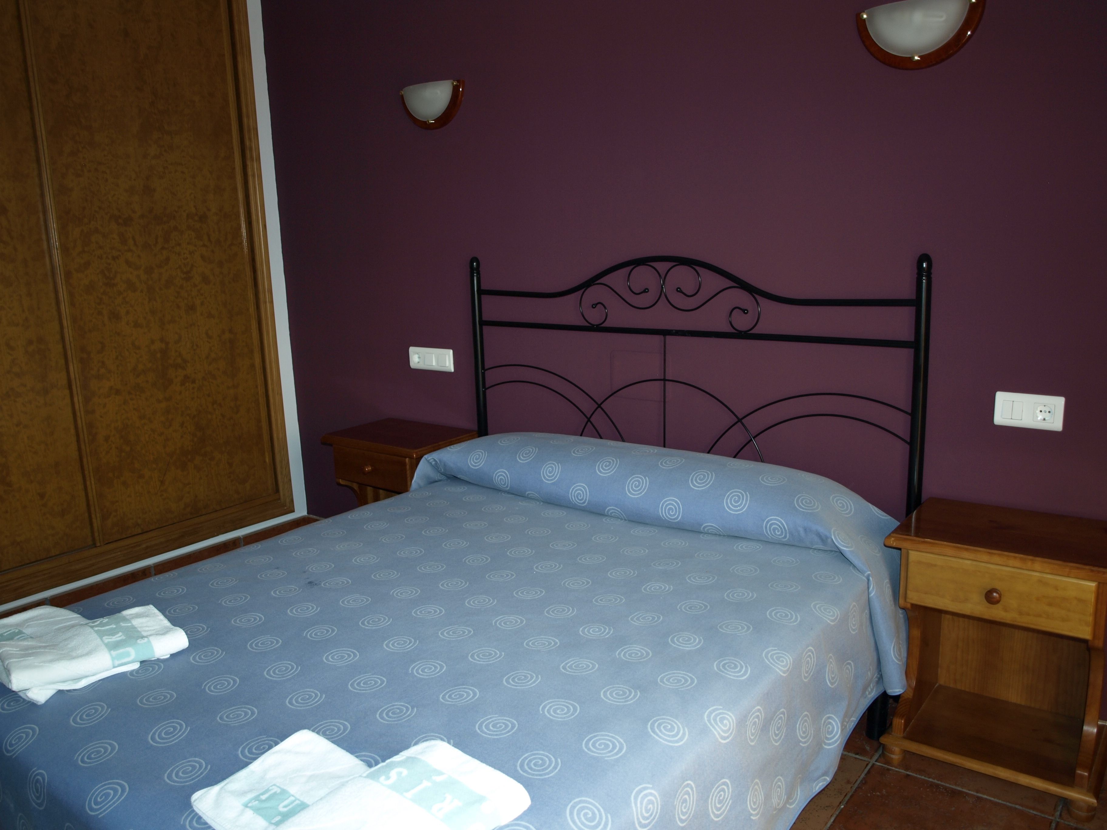 Un dormitorio con cama, mesitas de noche, armario y apliques.