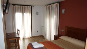 A hotel room with a bed, a desk, a chair, and curtains. - Hotel El Churron (Sabinanigo)