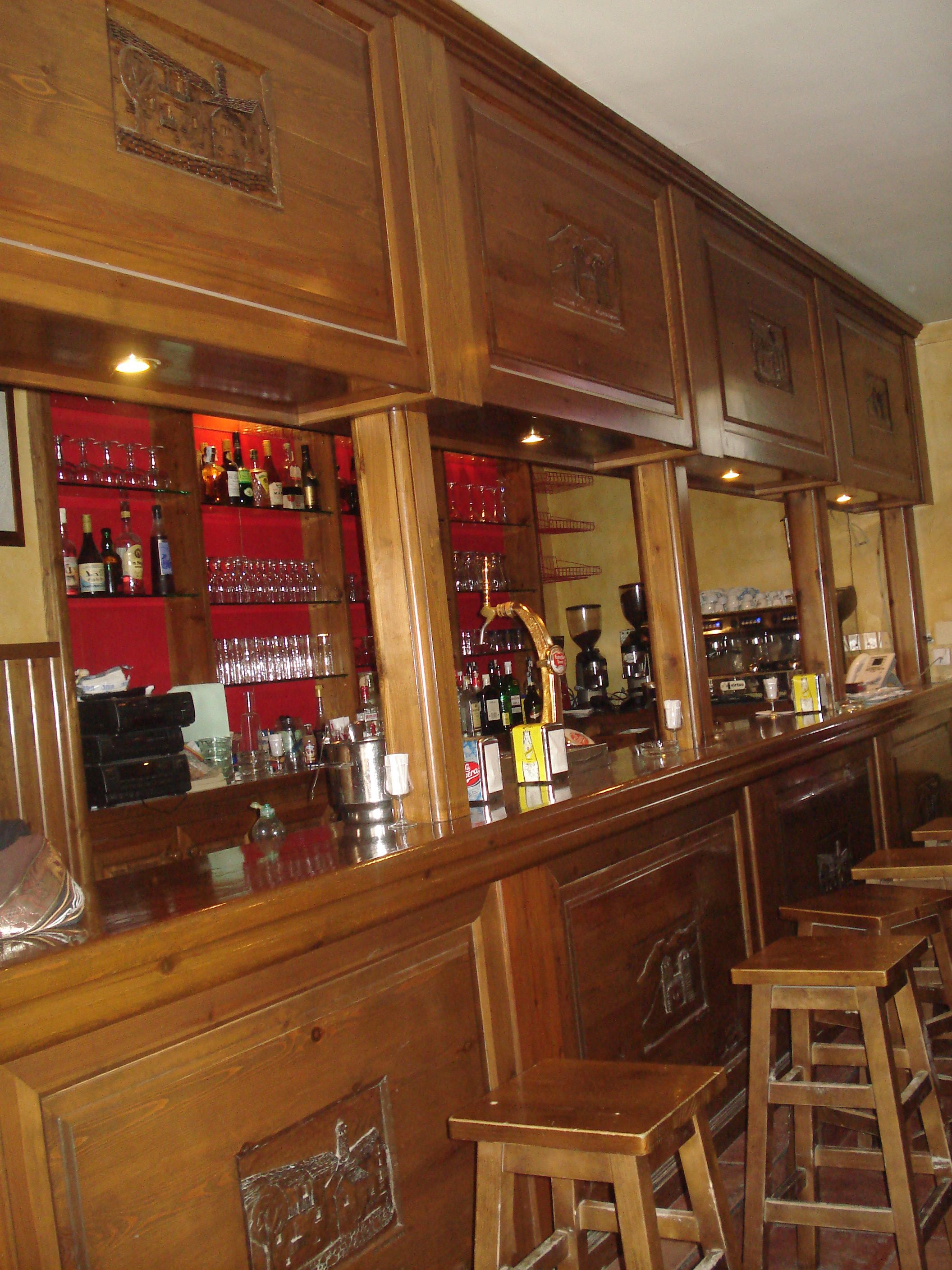 A bar area with wooden cabinets, shelves with bottles and glasses, and stools.