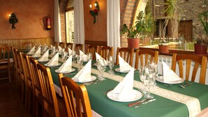 A dining area with a long table set for a meal, wooden chairs, and potted plants. - Hotel El Churron (Sabinanigo)