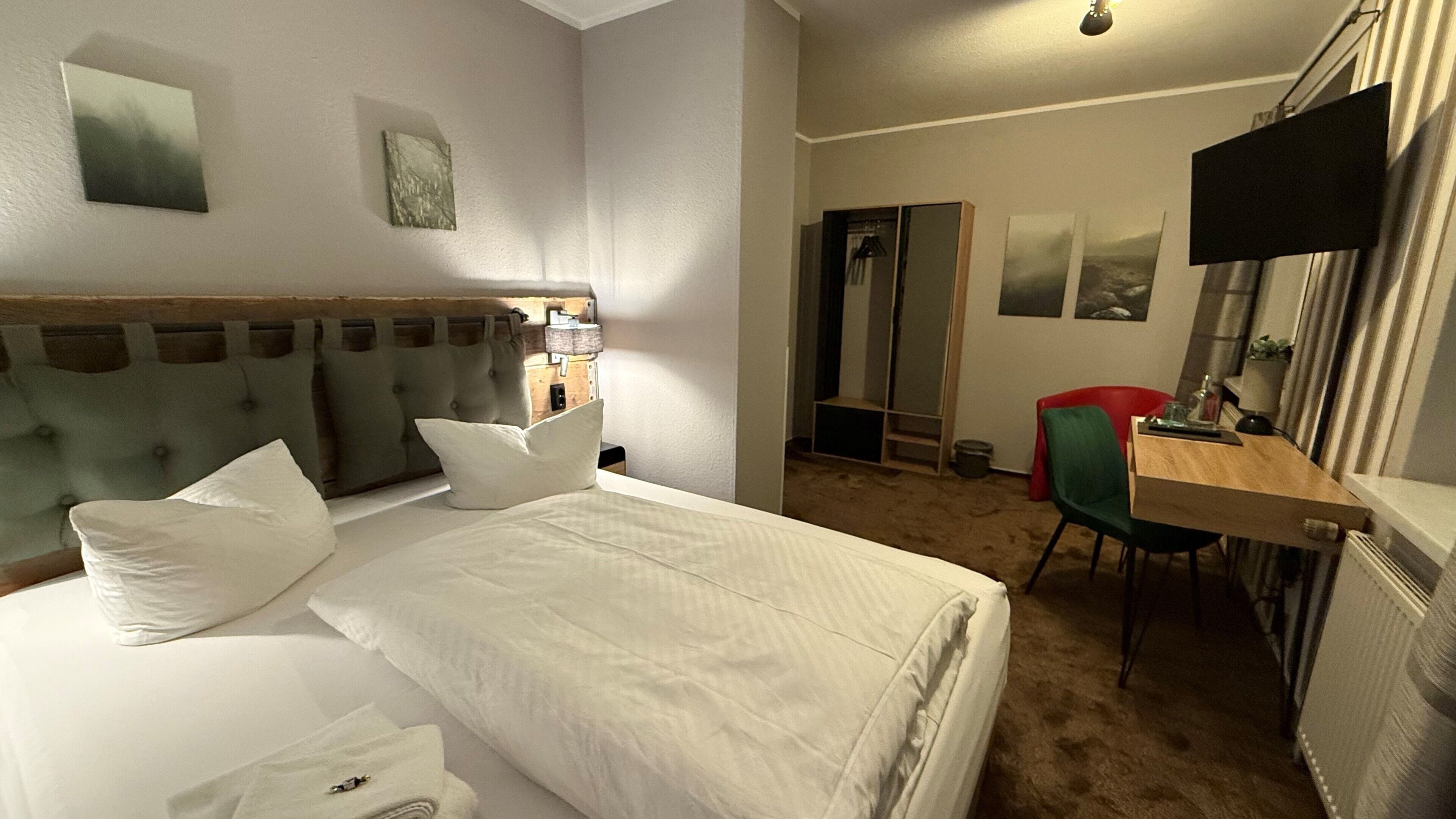 A hotel room with a bed, a desk, a chair, a TV, and artwork on the walls.