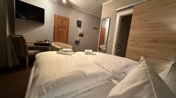 A hotel room with a large bed, a desk with a chair, a flat-screen TV mounted on the wall, and a wooden wardrobe. - Hotel Annablick (Strausberg)