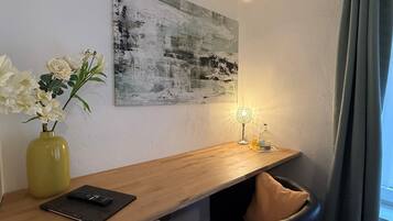 Quarto moderno com uma escrivaninha de madeira, um vaso com flores, uma luminária e um quadro na parede.