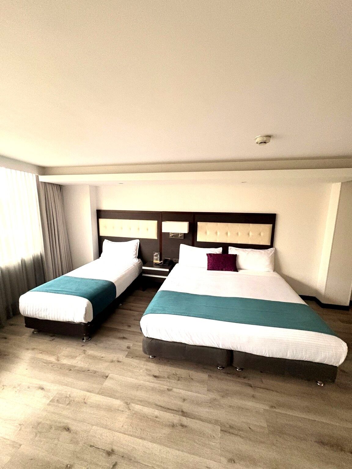 Una camera d'albergo con due letti, una testiera, un comodino e una finestra con tende.