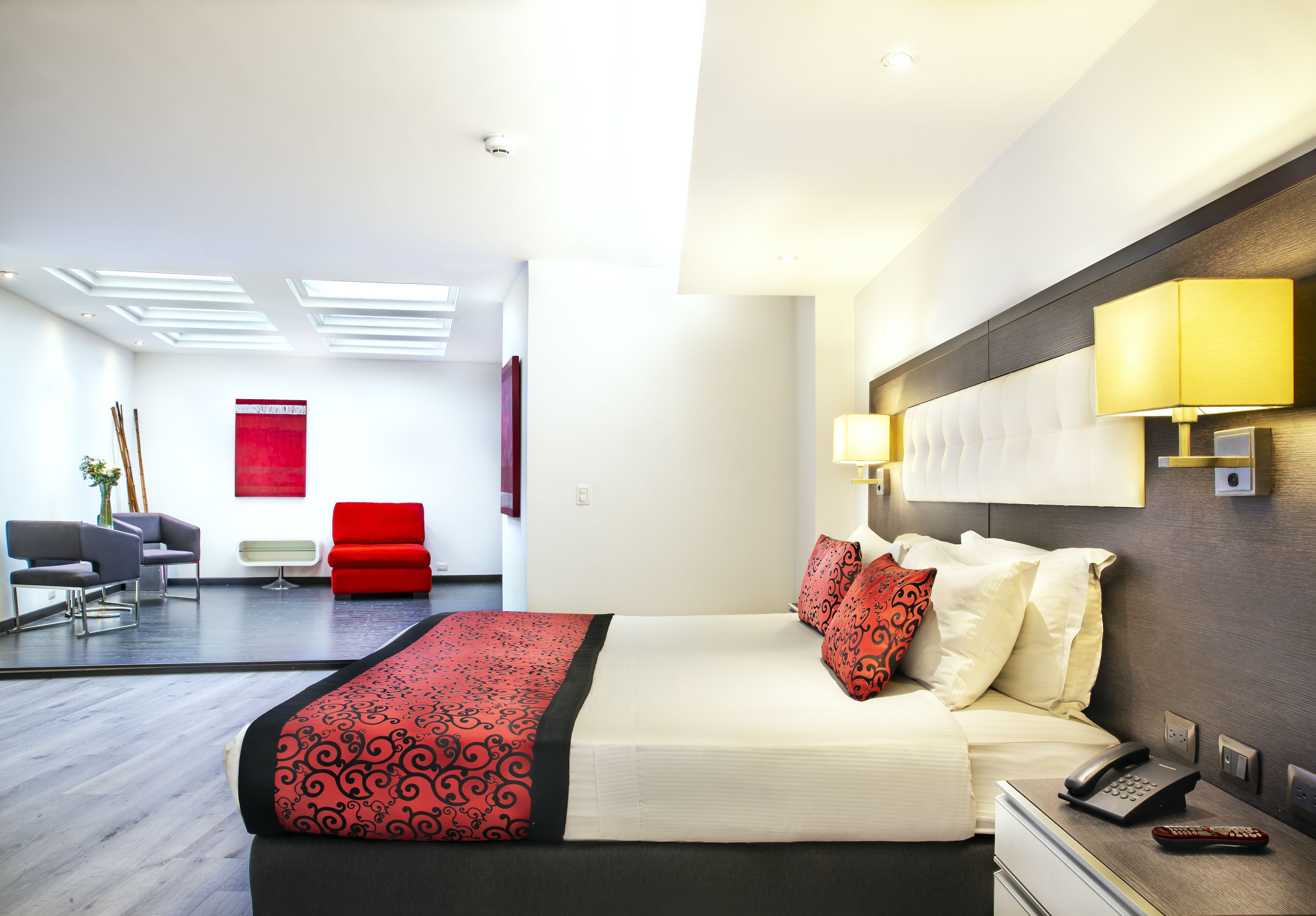 A modern hotel room with a large bed, bedside lamps, a telephone, and a desk with a lamp.