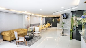 A modern lobby with a sofa, chairs, a reception desk, and a TV screen.