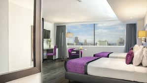 A hotel room with a large bed, a desk, a chair, and a view of the city skyline.