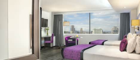 A hotel room with a large bed, a desk, a chair, and a view of the city skyline.
