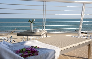 A balcony with a view of the sea, a bed with a towel and a flower, and a small table with a vase and a cup. - Hotel Le Soleil (Jesolo)