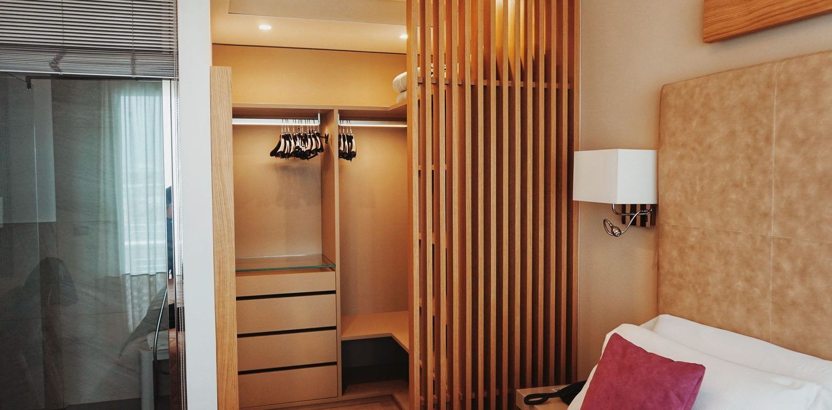 Quarto de hotel com closet espaçoso, cama, luminária de cabeceira e área de chuveiro.