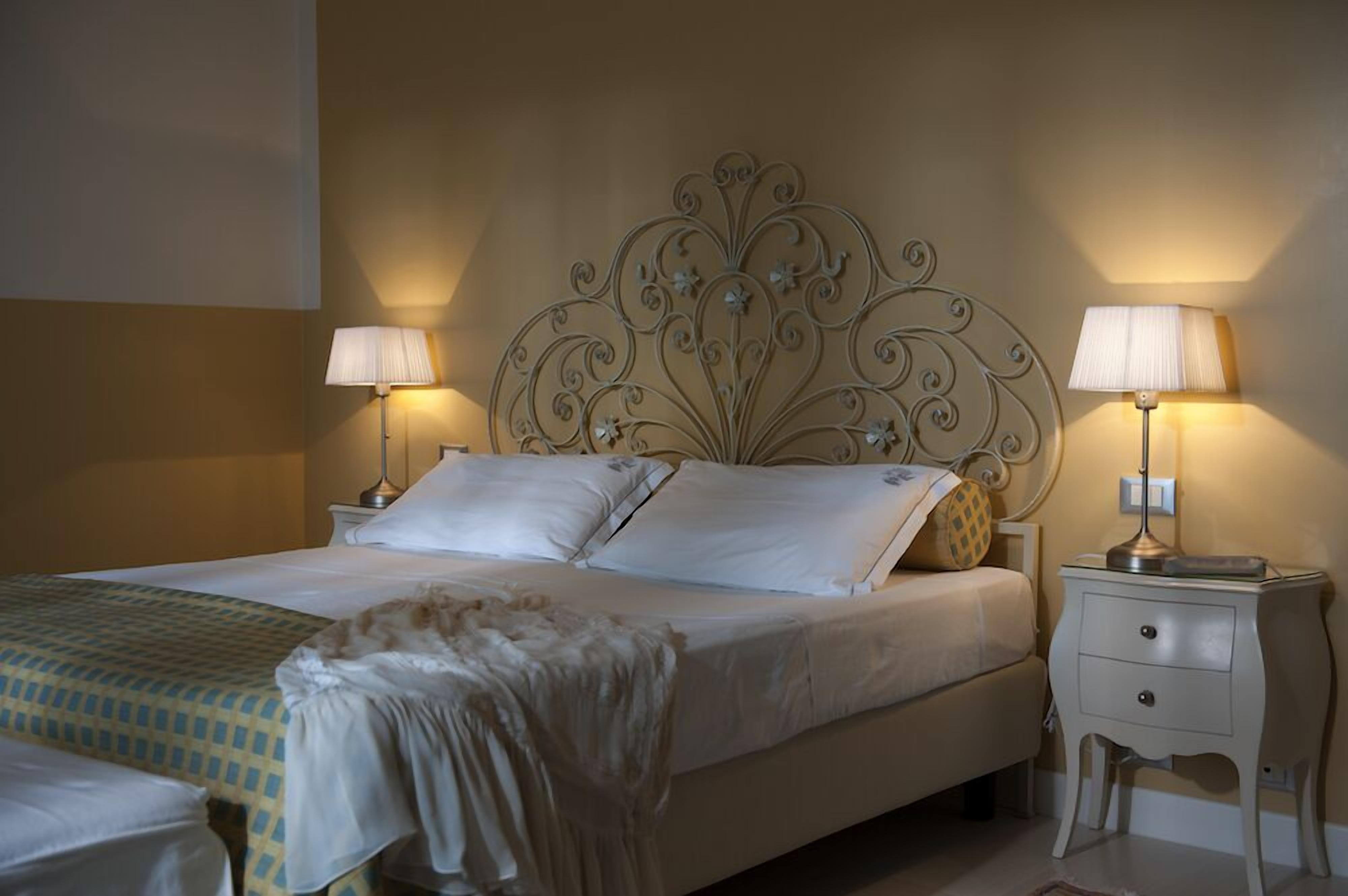 A neatly made bed with white linens and a decorative headboard, flanked by two bedside tables with lamps.