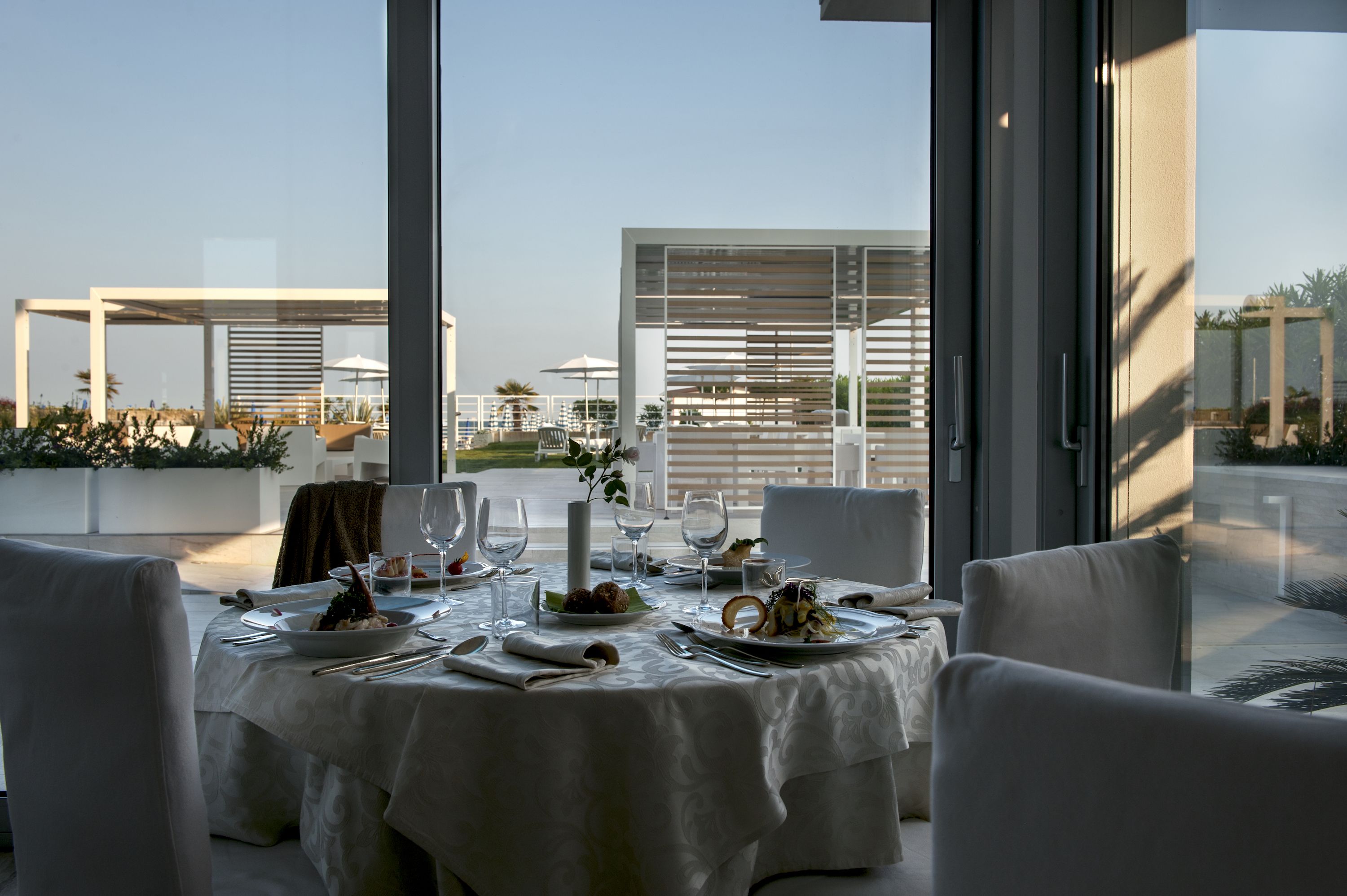 A dining table set for two with a view of a modern building and a garden.