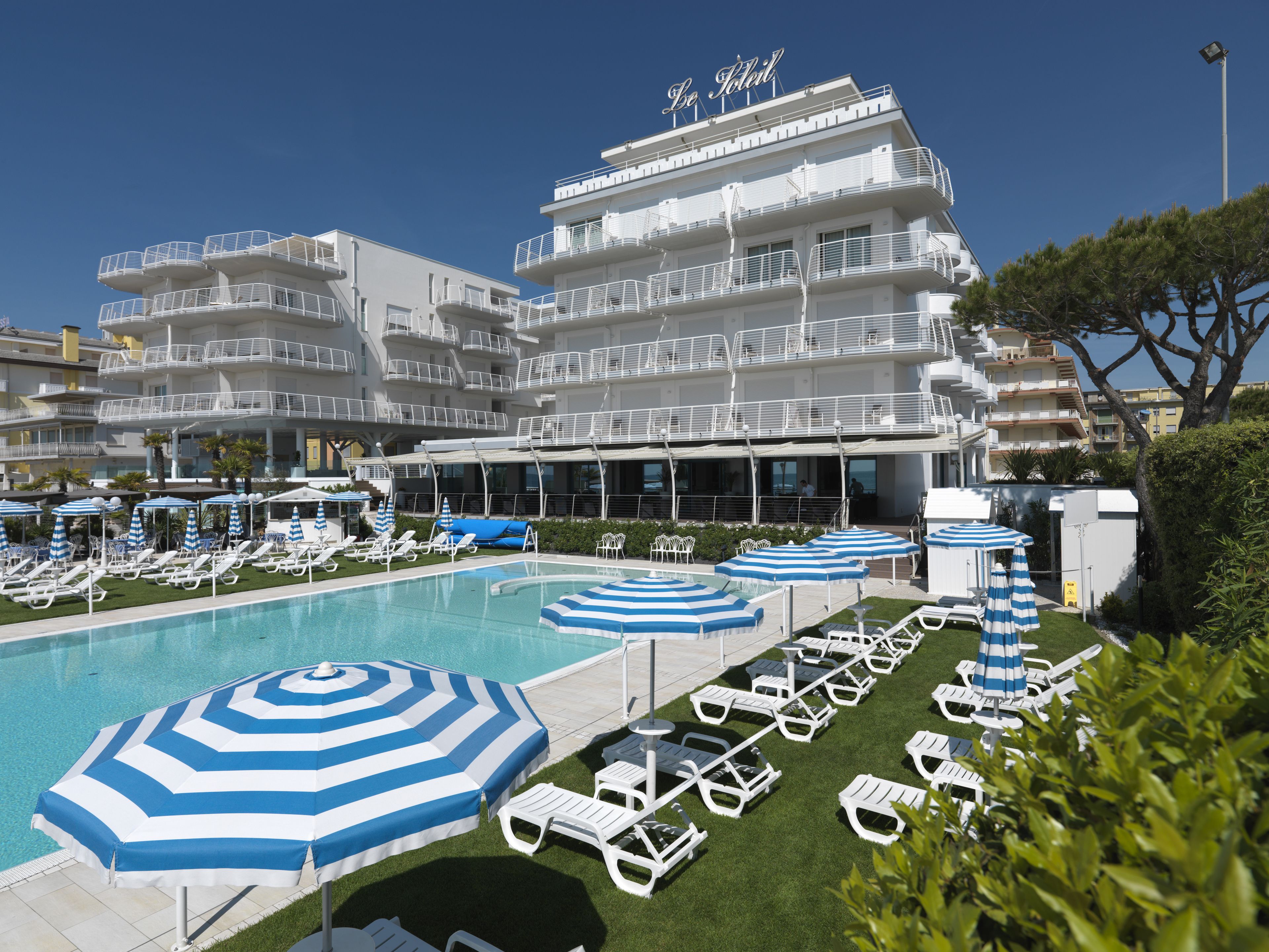 Un hotel con zona de piscina, varios balcones y mobiliario exterior con sombrillas.